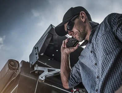 Worker using a handheld two-way radio beside heavy equipment
